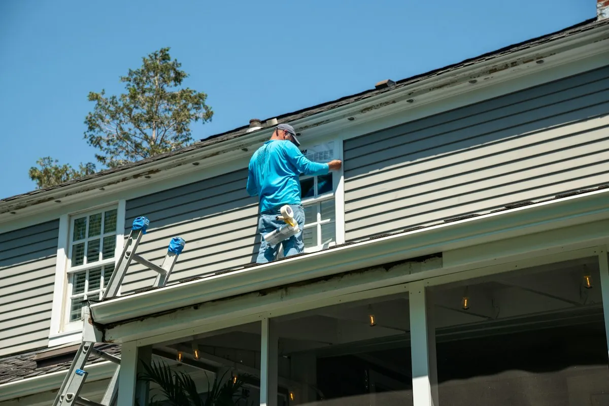 Contractor on a porch roof repairing gray lap siding around a window